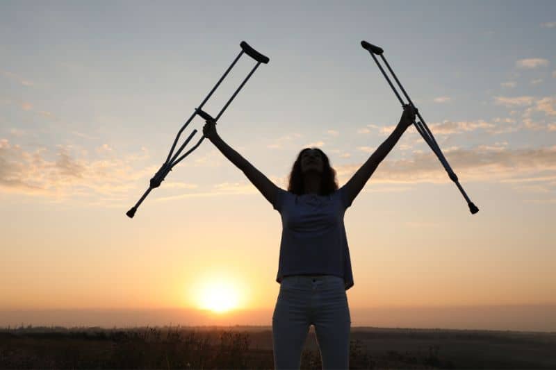 A silhouette of a woman holding crutches in her hands